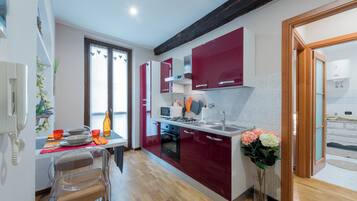A modern kitchen with red cabinets, a wooden floor, and a dining area with a table and chairs.