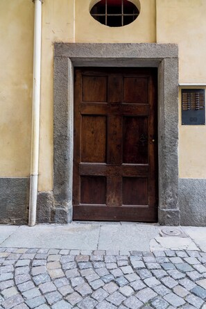 Une grande porte en bois, encadrée de pierre, est intégrée à un bâtiment dont le mur est jaune et qui possède une petite fenêtre au-dessus.