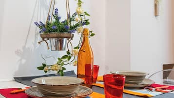 A dining table with plates, bowls, and a bottle, set with orange napkins and red glasses.