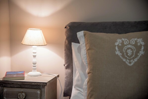 A bedside table with a lamp, a book, and a pillow with a heart design.