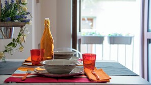 Een eettafel gedekt met borden, kommen en glazen, met een fles en een bloemstuk ernaast.