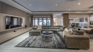 A modern living room with a sectional sofa, a coffee table, and a TV mounted on the wall. - Khaya Elihle Guest House (Sabi River Eco Estate)