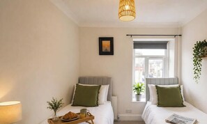 A hotel room with two beds, a window with a view, a bedside table with a lamp, and a picture on the wall.