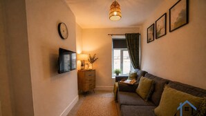 A cozy living room with a sofa, a TV mounted on the wall, a wooden cabinet, a lamp, and a window with curtains. - Barret Flat, sleeps 4, central location, Penarth (Penarth)