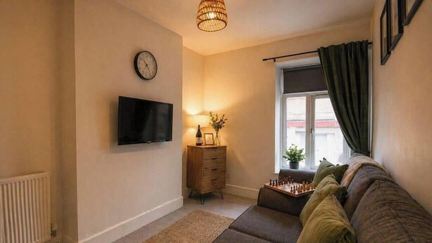 A cozy living room with a flat-screen TV, a wooden side table with a lamp, a chessboard, and a window with curtains. - Barret Flat, sleeps 4, central location, Penarth (Penarth)