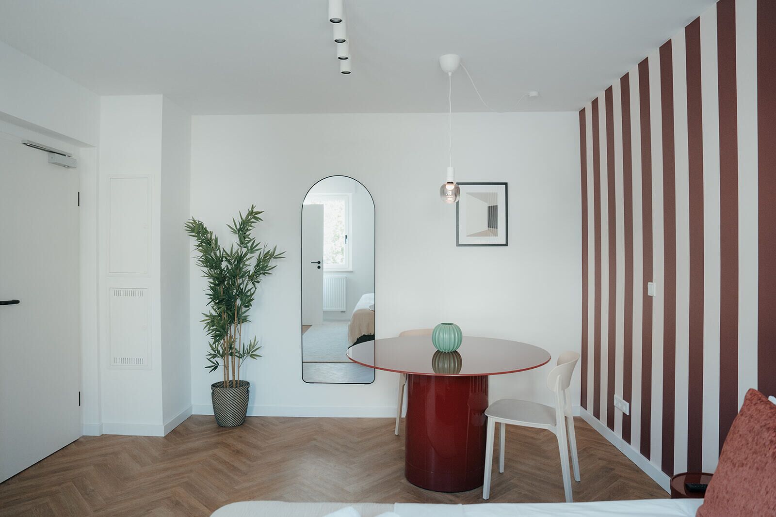 Un interior moderno con un comedor que presenta una mesa redonda, una planta en maceta y un espejo.