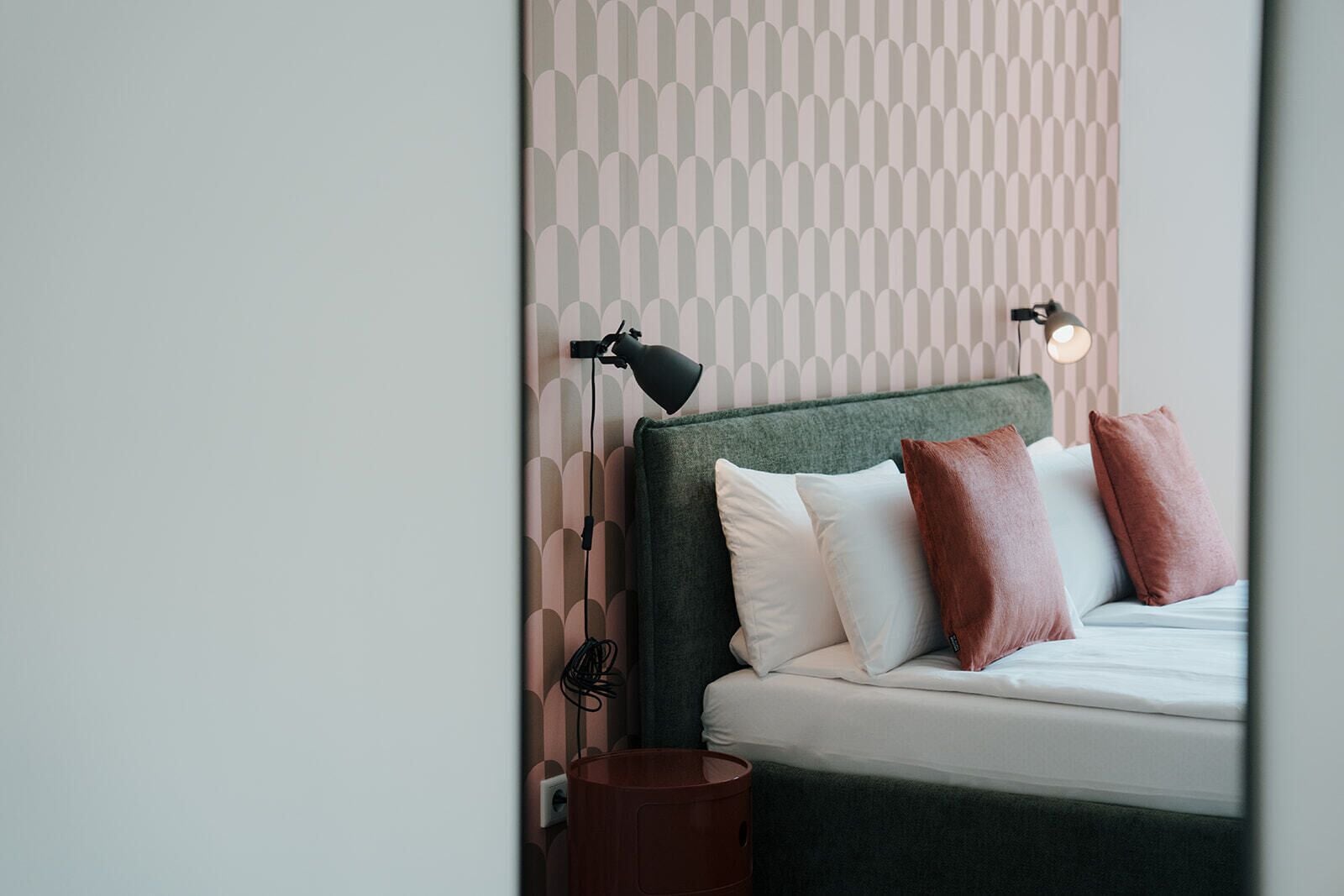 A neatly made bed with pillows, a bedside lamp, and a wall with a geometric pattern.
