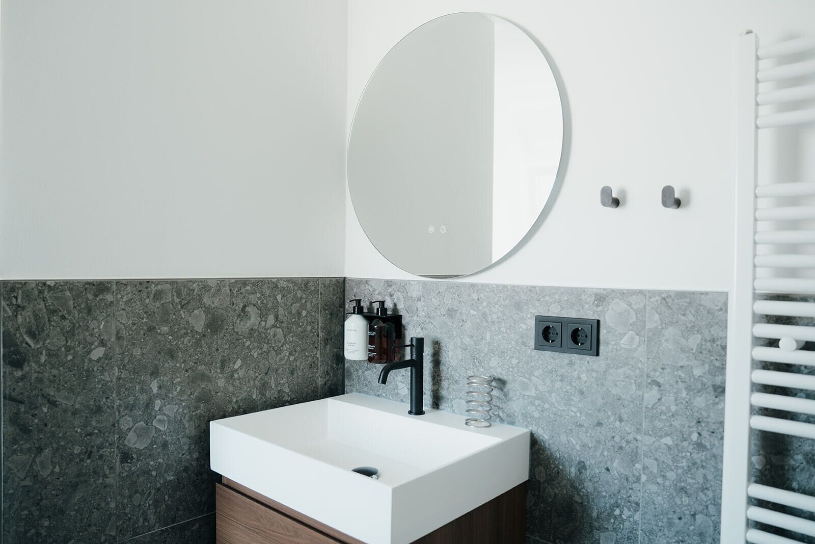 A bathroom with a white sink, a round mirror, and a towel rack.