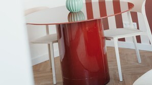 A modern room with a red glass table, white chairs, a framed picture, and a striped wall.