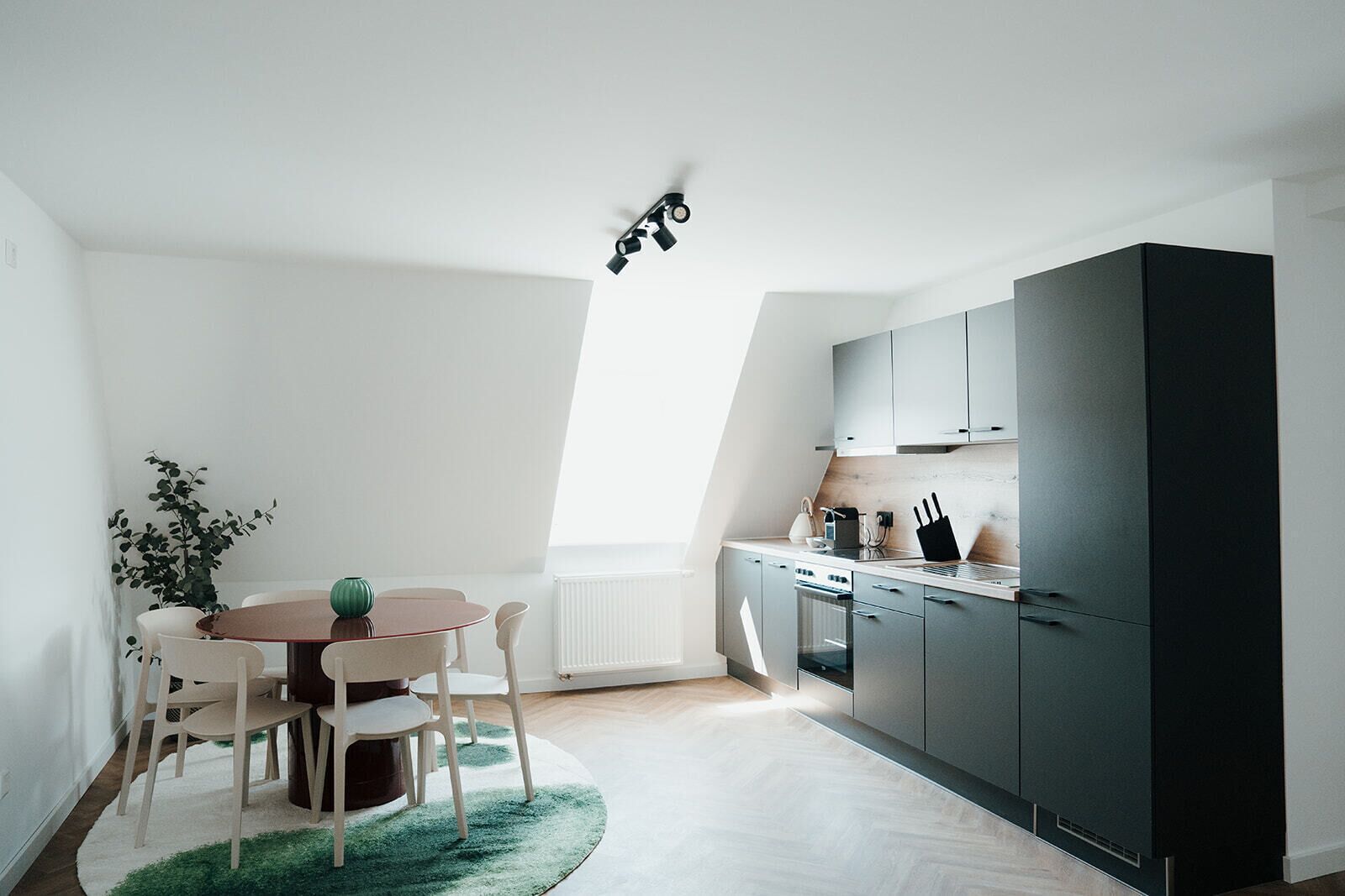 Una cucina moderna con zona pranzo, che include un tavolo rotondo, sedie, un termosifone e un frigorifero nero.