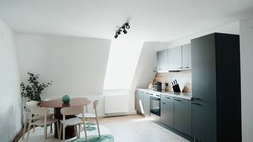 Una cucina moderna con zona pranzo, che include un tavolo rotondo, sedie, un termosifone e un frigorifero nero.