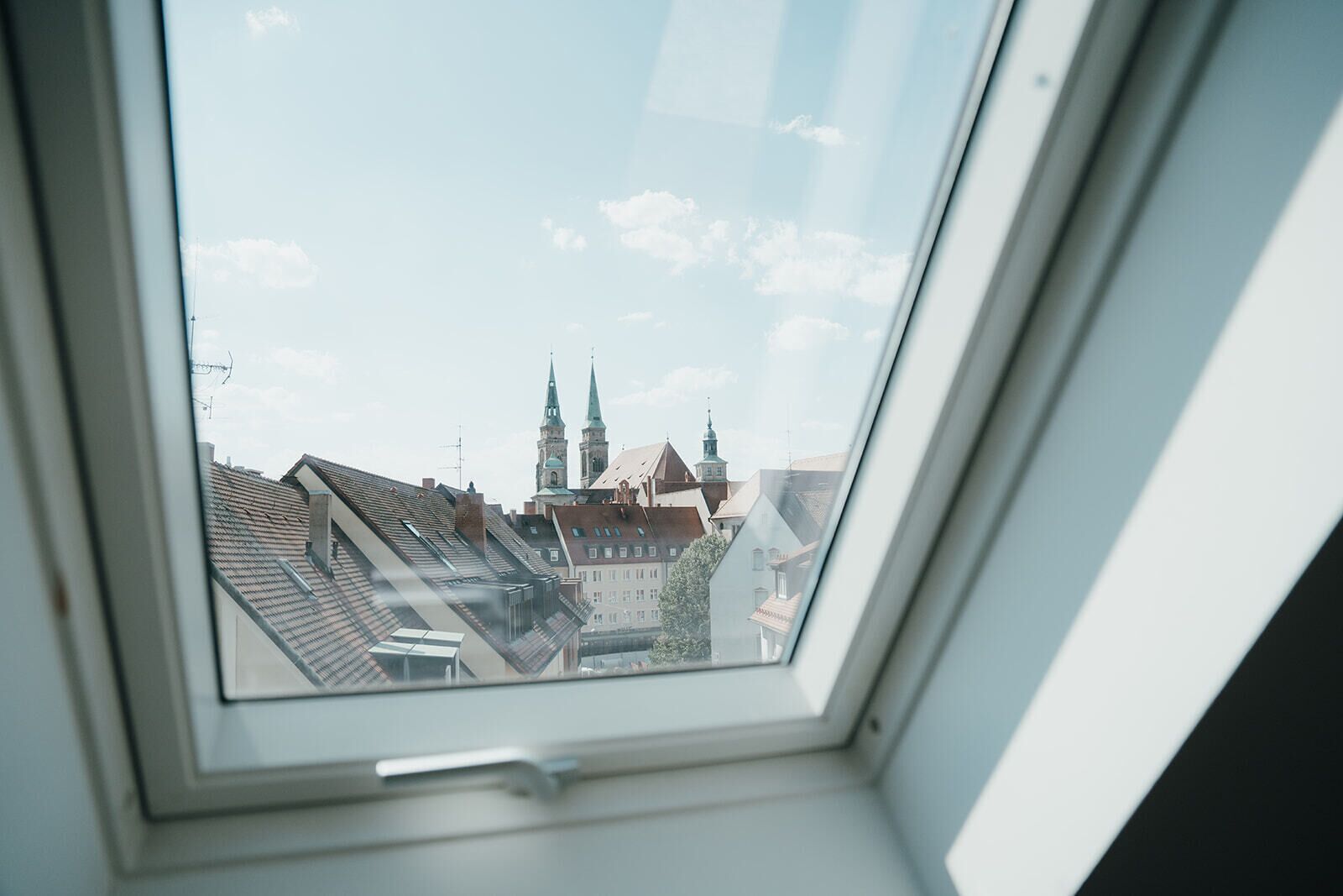A skylight window with a view of a cityscape, including buildings and a church with two spires.