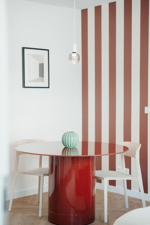 Un coin repas avec une table ronde, deux chaises, un vase, une suspension et un mur à rayures.