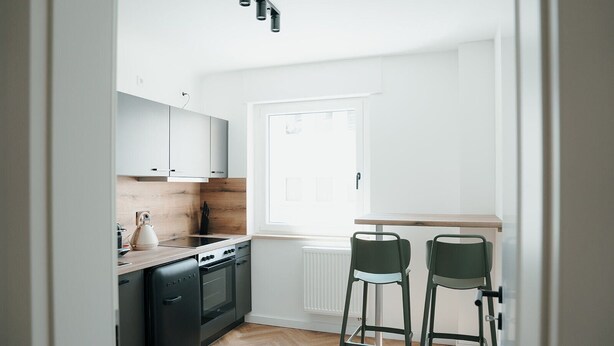A compact kitchen with a dishwasher, stove, and two bar stools.