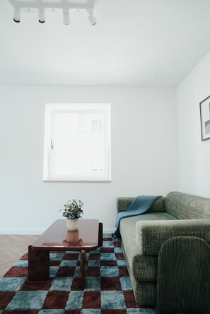 Un salon avec un canapé, une table basse, une plante en pot et un tapis à motifs.
