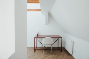 A small, modern room with a wooden floor, a white chair, and a simple desk with a lamp. - The Haus HANS Nürnberg (Nürnberg)