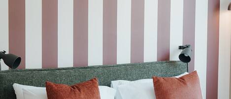 A neatly made bed with white linens and two brown pillows, a green headboard, and a striped wall in the background.