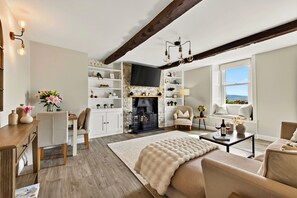 Ein geräumiges Wohnzimmer mit Kamin, Holzbalken und Blick durch ein großes Fenster.
