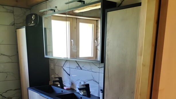 Un baño con suelo de mármol, un lavamanos negro y un tocador de madera con un espejo arriba.