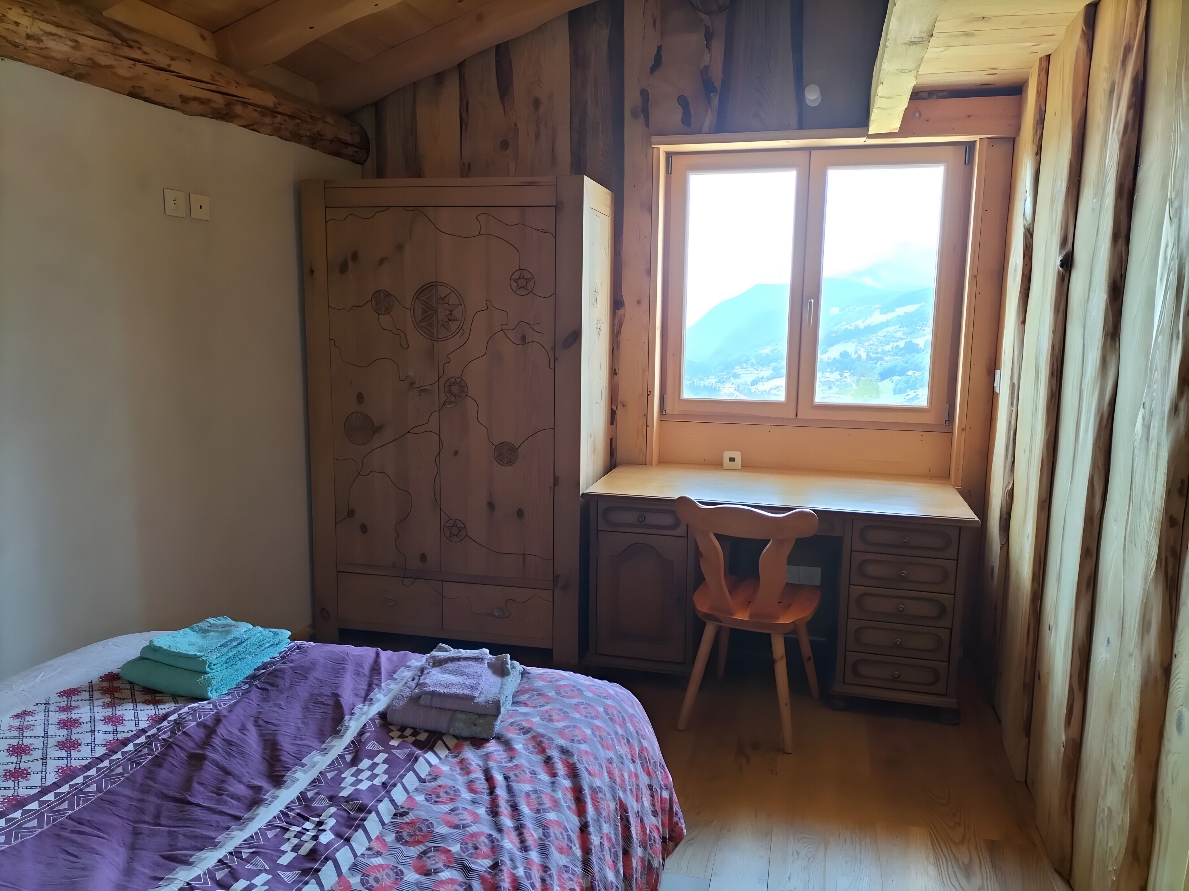 Un dormitorio con cama, escritorio y silla, armario y ventana con vistas.