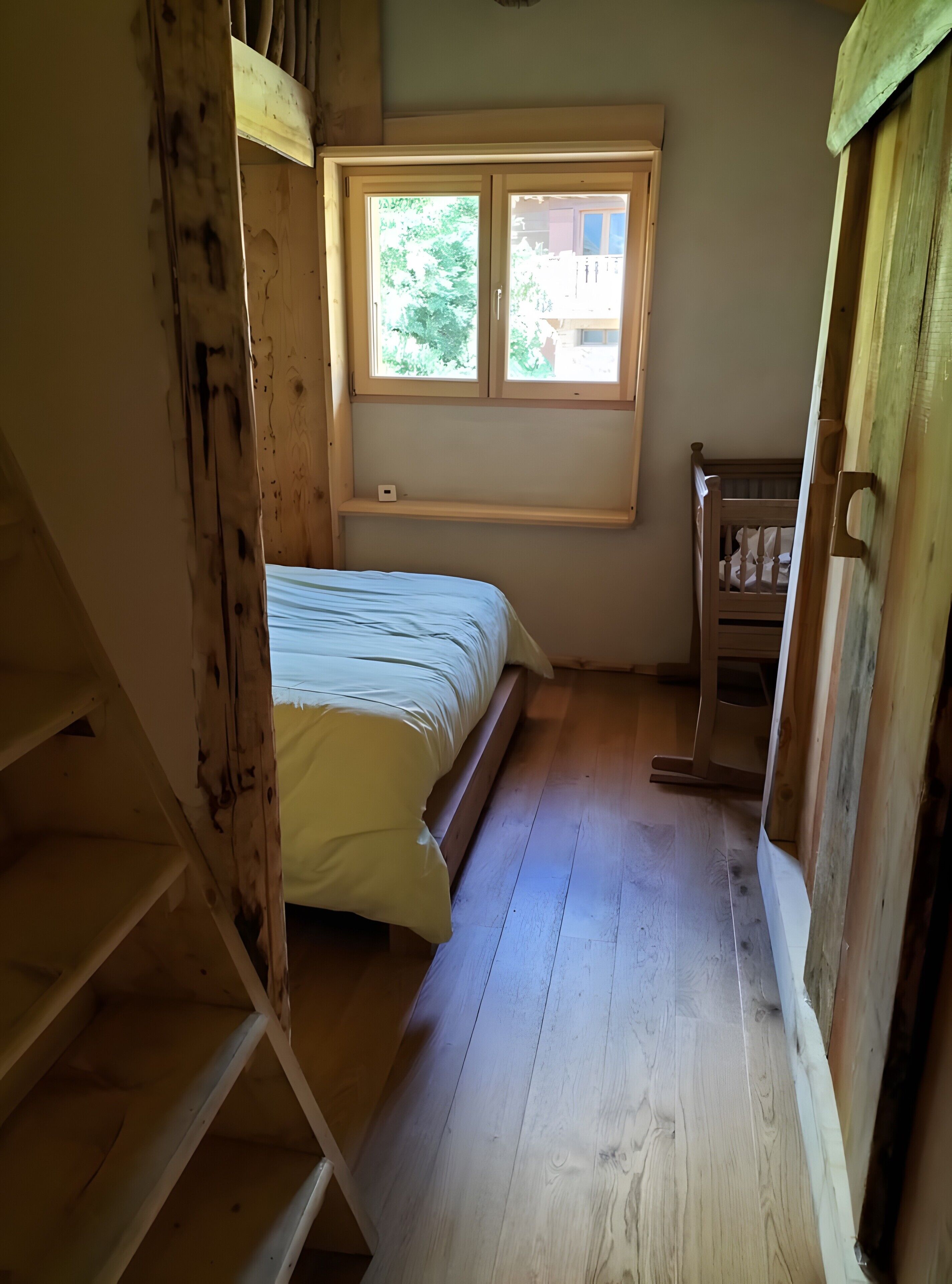 Une pièce comprenant un lit, une fenêtre, un escalier en bois et une petite commode en bois.