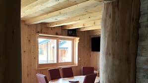 Interior de madera con una mesa redonda y sillas, una ventana y un televisor montado en la pared.