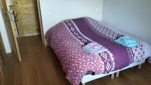 Una cama individual con una colcha estampada, una manta doblada y un almohadón sobre un suelo de madera.
