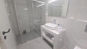 Un baño moderno con ducha de vidrio, lavamanos blanco y espejo encima.