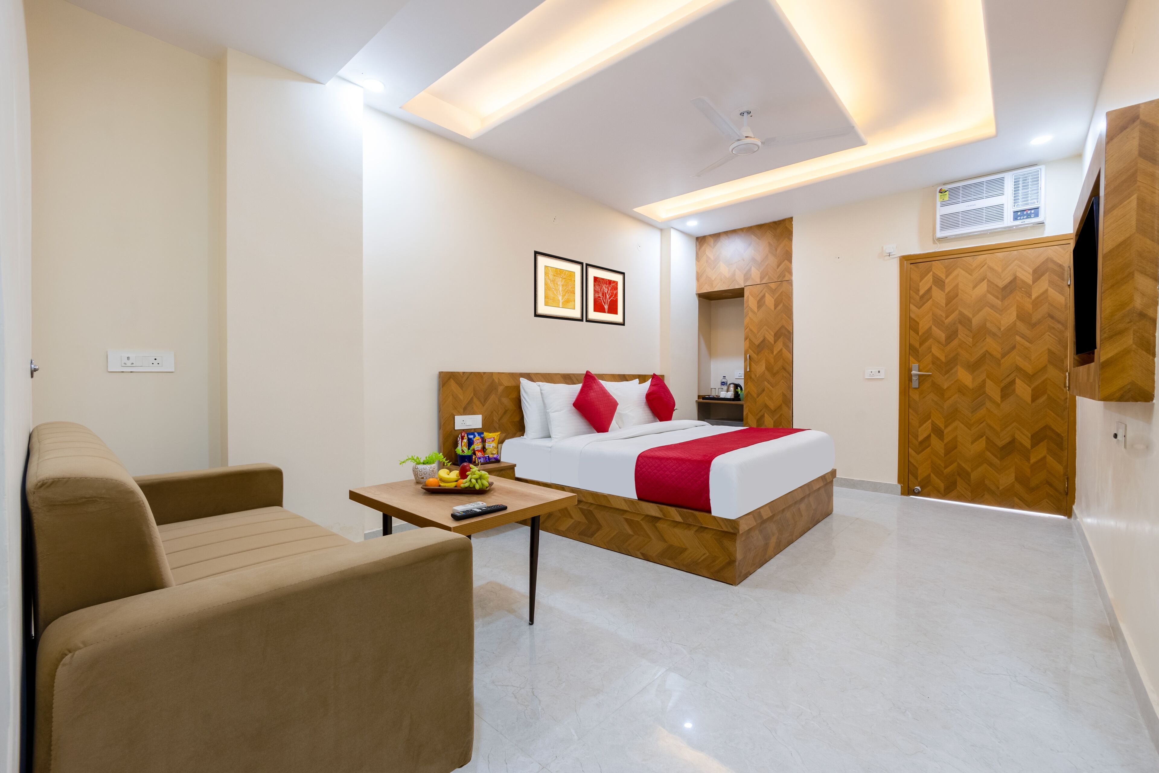 A hotel room with a bed, a sofa, a small table with snacks, and a TV.