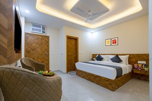 A modern bedroom with a bed, a chair, a bedside table with snacks, and a ceiling fan. - Castle Prime (New Delhi)