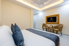Habitación de hotel con cama, escritorio, dos sillas, cafetera y un logo enmarcado en la pared.