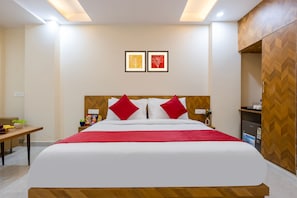 A hotel room with a bed, a bedside table, a small desk, and a wardrobe. - Castle Prime (New Delhi)
