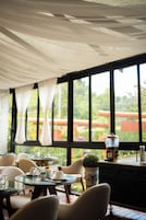 A dining area with tables, chairs, and a view of greenery outside.