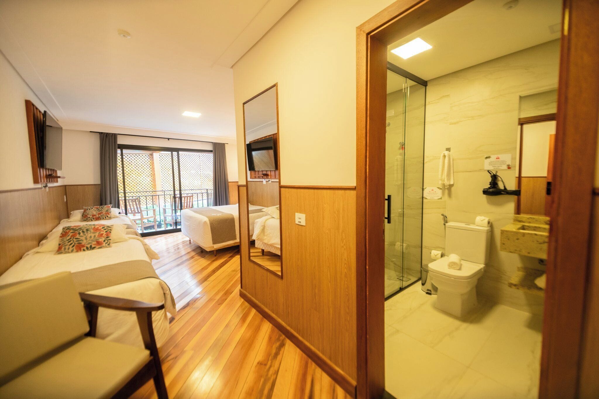 Quarto de hotel com varanda, cama, sofá, televisão e banheiro com vaso sanitário e chuveiro.