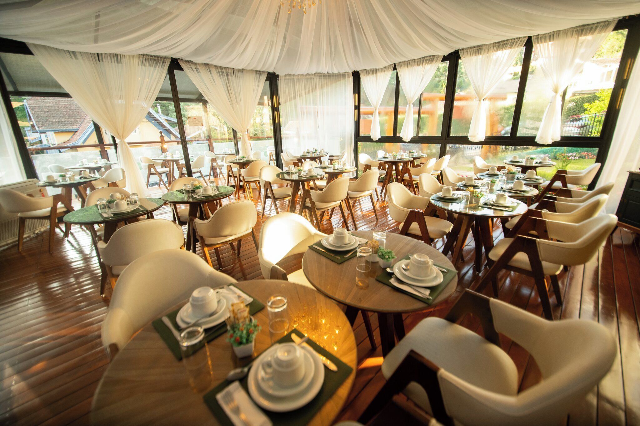 Um restaurante com mesas e cadeiras redondas, amplas janelas e vista para o exterior.