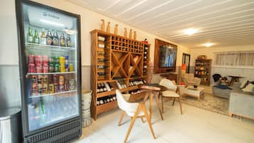 Uma sala de estar com adega, geladeira com bebidas, televisão e assentos.
