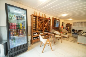 Uma sala de estar com adega, geladeira com bebidas, televisão e assentos.