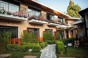 A two-story building with a brick facade, balconies with flower boxes, a stone pathway, and a wooden fence.