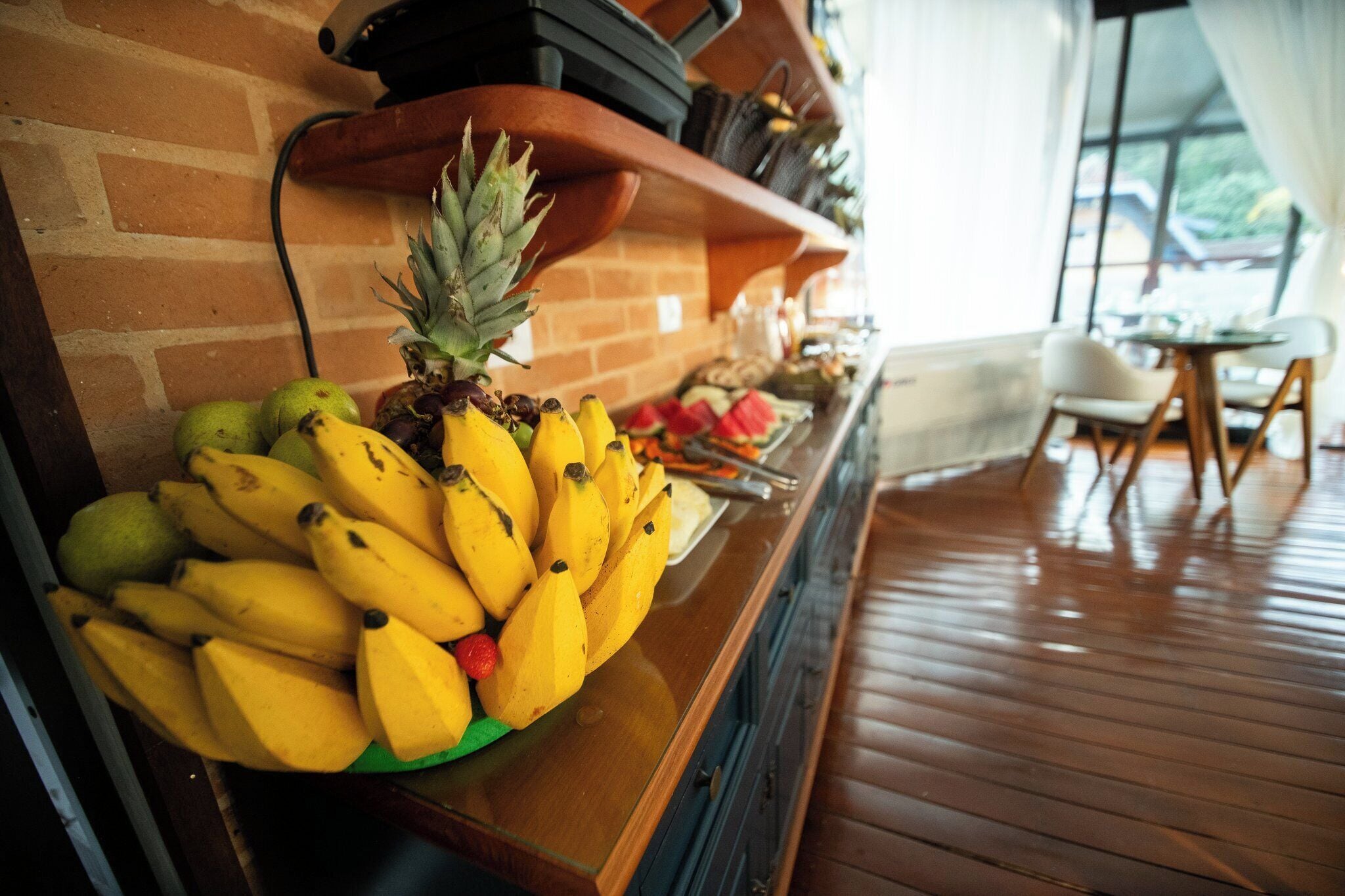 A wooden counter with a fruit display including bananas and a pineapple.
