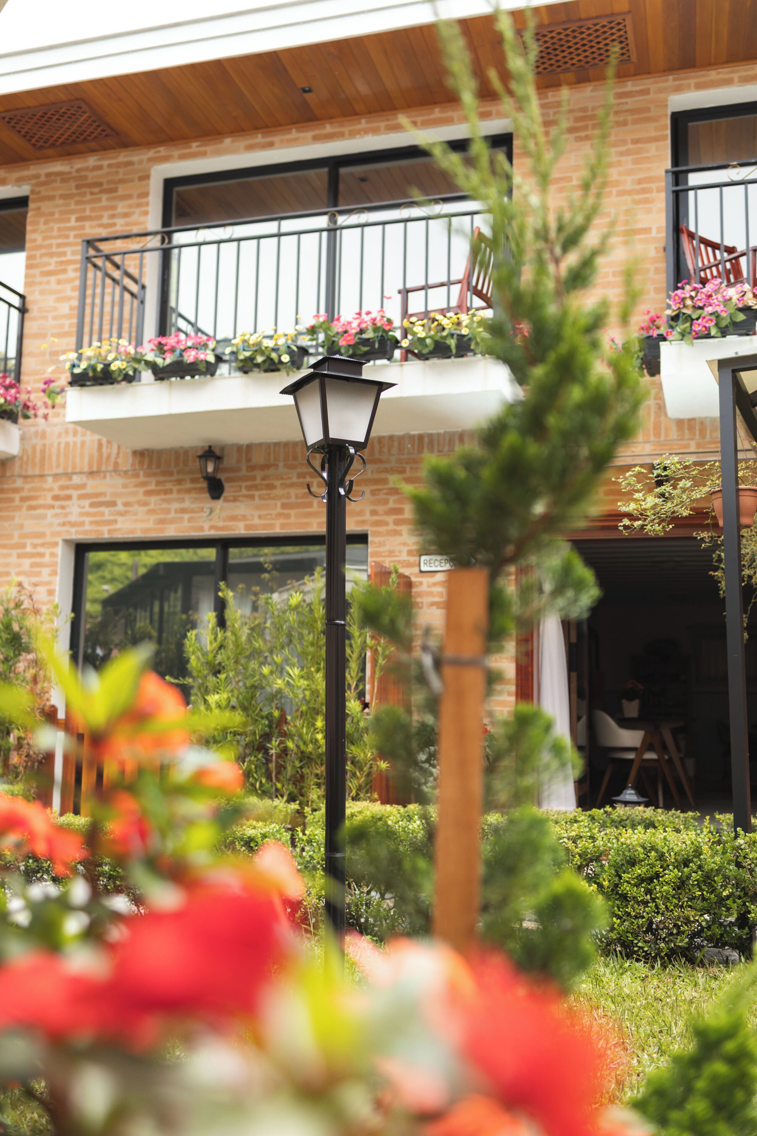 Un edificio con fachada de ladrillo, un balcón con plantas en macetas y una farola.