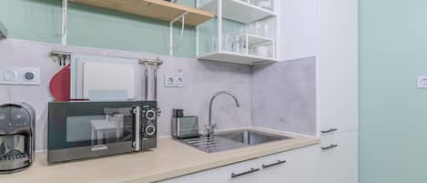 A compact kitchen with a microwave, toaster, and coffee maker on the counter, a sink, and a cabinet with a built-in oven.