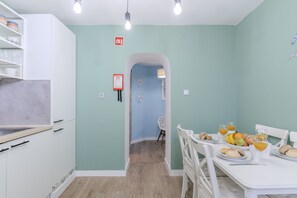 A kitchen with white cabinets, a dining table set with fruits and glasses, and a blue wall with a fire safety sign. - #414 Central Apartment | Walking Distance to the Beach (Albufeira)