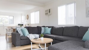 A modern living room with a sectional sofa, a round coffee table, and a dining area with a white table and chairs. - 'Sopra'  Shoal Bay - Close to the beach (Shoal Bay)