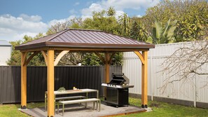 Ein hölzerner Pavillon mit einem Metalldach, einem Grill und einem Picknicktisch mit Bänken.