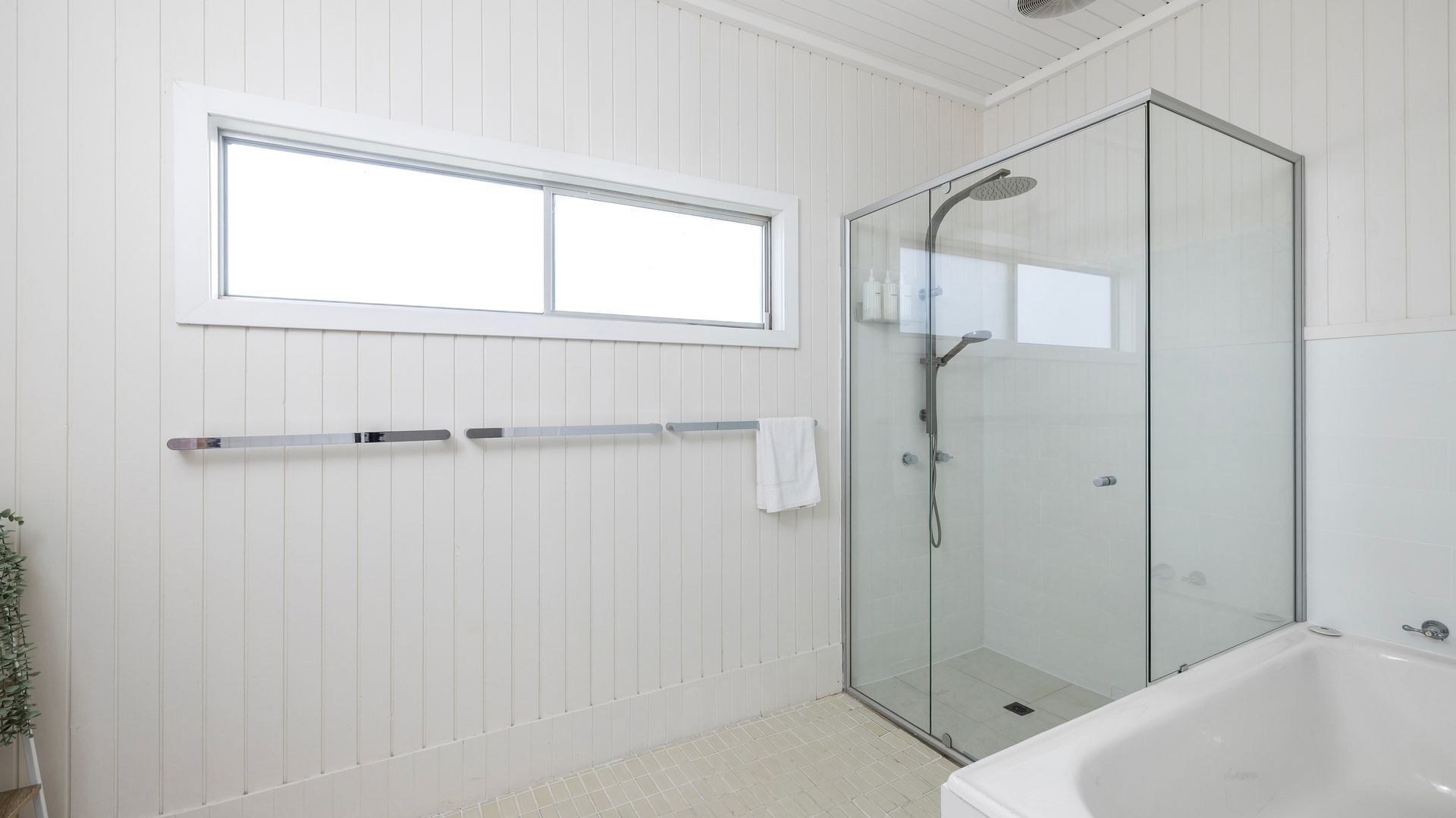 A bathroom with a glass-enclosed shower, a bathtub, and a window above the shower.