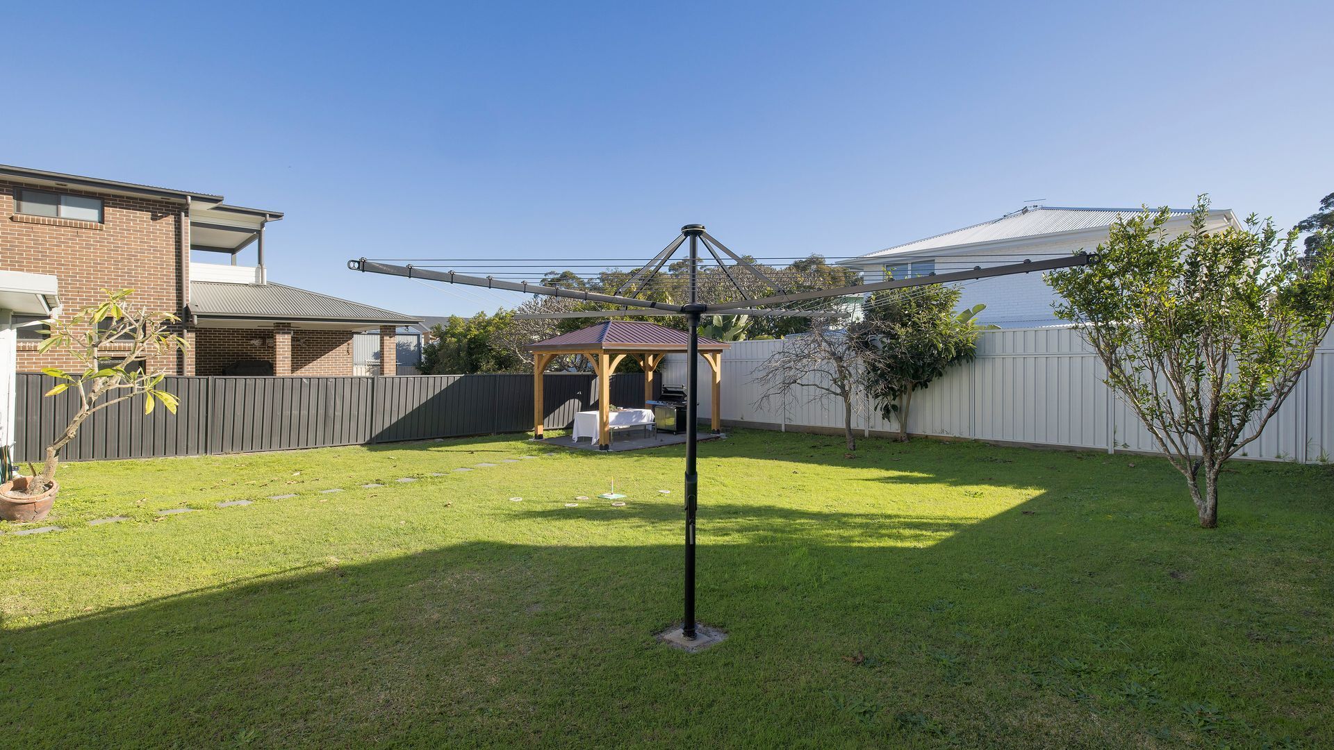 A backyard with a grassy lawn, a barbecue area, a wooden pergola, and a metal structure.
