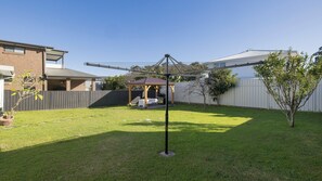 Ein Garten mit Rasen, Grillplatz, einer Holz-Pergola und einer Metallkonstruktion.