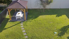 Een achtertuin met een overdekte patio, een barbecue en een kleine boom.