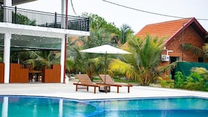 Une piscine entourée de palmiers et d’un bâtiment au toit rouge, avec des chaises longues et des parasols à proximité.