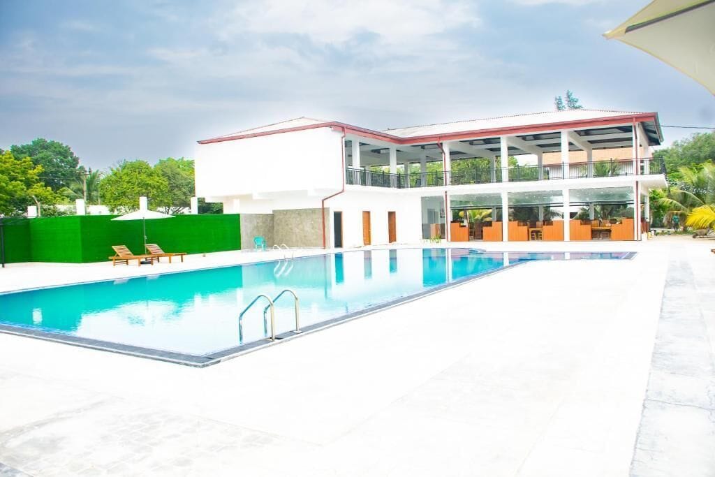 A modern building with a pool, a covered outdoor area, and a green fence.